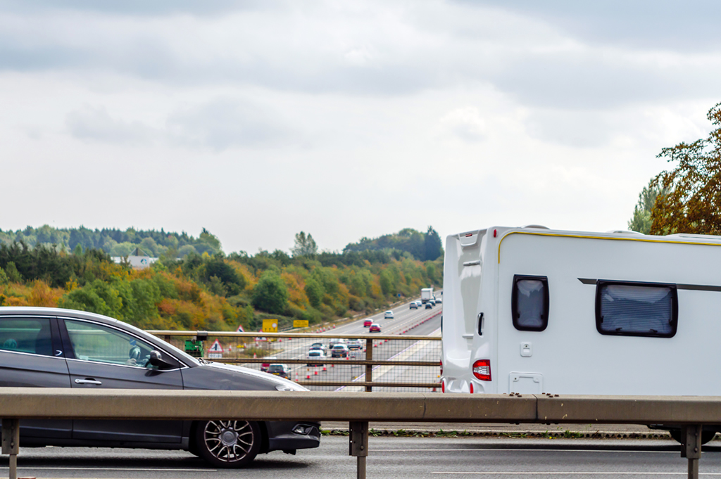 Car behind a caravan on a bridge above the motorway 