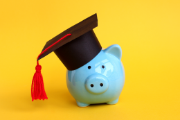 small blue piggy bank with a black mortar board hat on its head against a yellow background