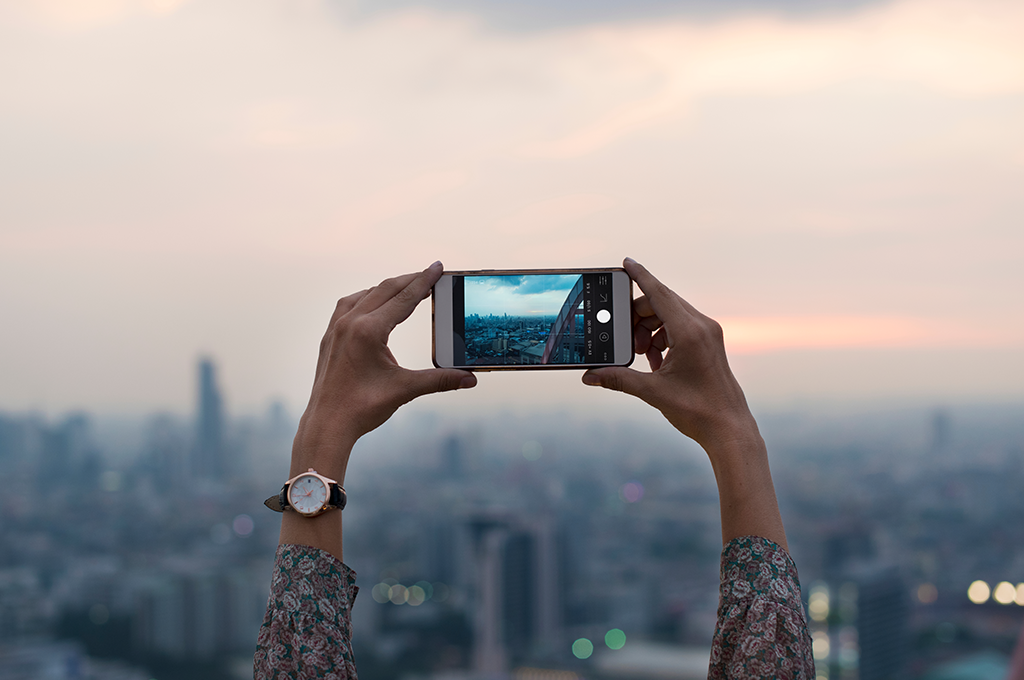 a woman is holding a smartphone above her head and is taking a photograph of a cityscape