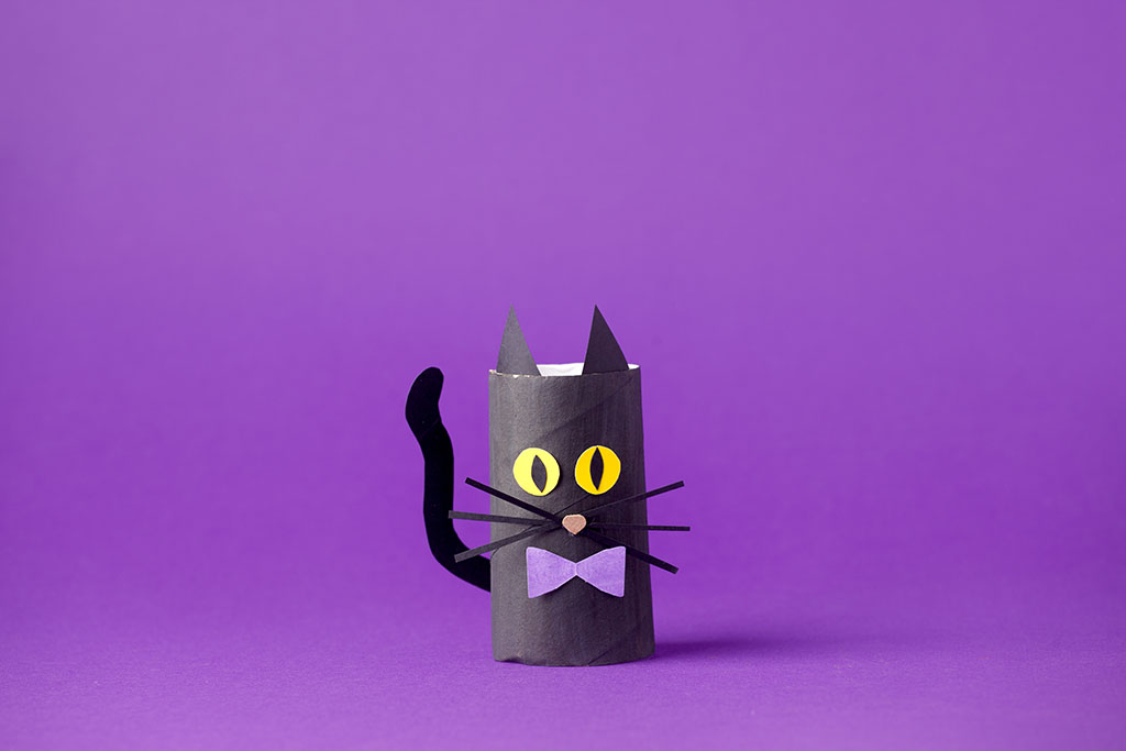 a black cat made out of a toilet roll cardboard tube on purple for Halloween