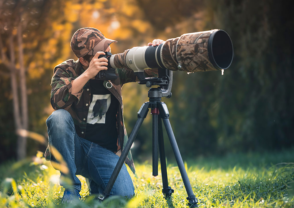 wildlife photographer using telephoto lens with camouflage coating photographing outdoors