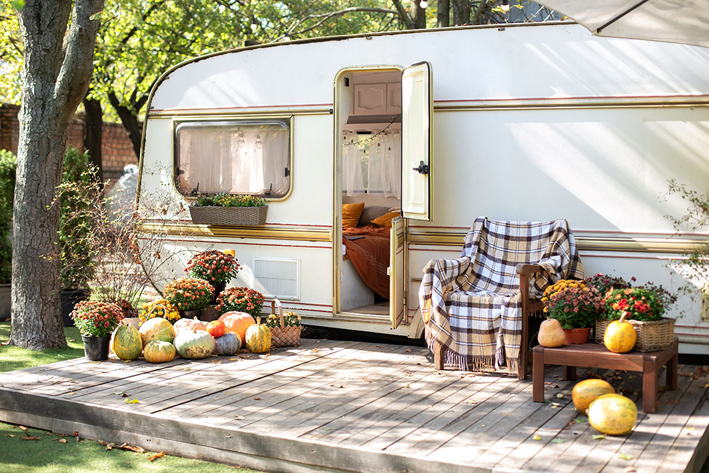 the exterior of a caravan on a sunny day with a decking that includes a seating area with pumpkins and flowers 