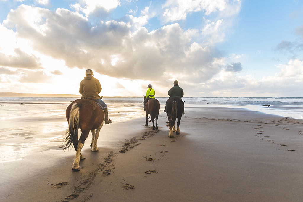 three people horse riding on the beach.
