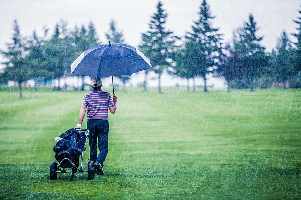 golfer on a rainy day leaving a golf course holding an umbrella over his head 