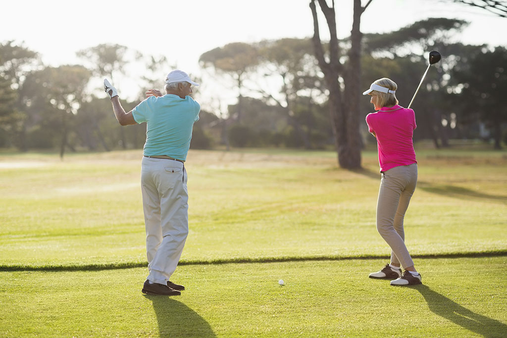 male golf player teaching a woman how to improve her swing while standing on the field