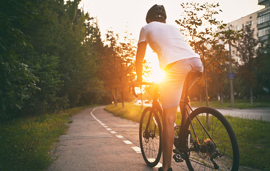 Man in casual clothes is cycling on the road at sunset 