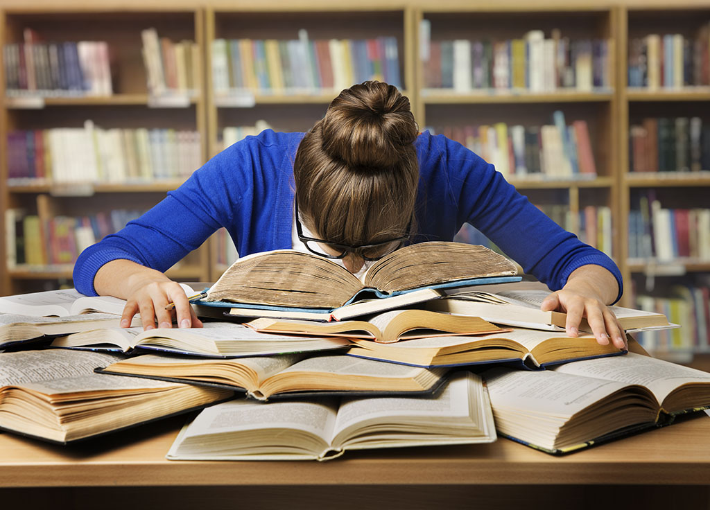 woman resting her head on a pile of books in the library 