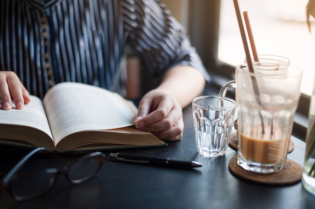Person reading a book with an iced coffee in a cafe
