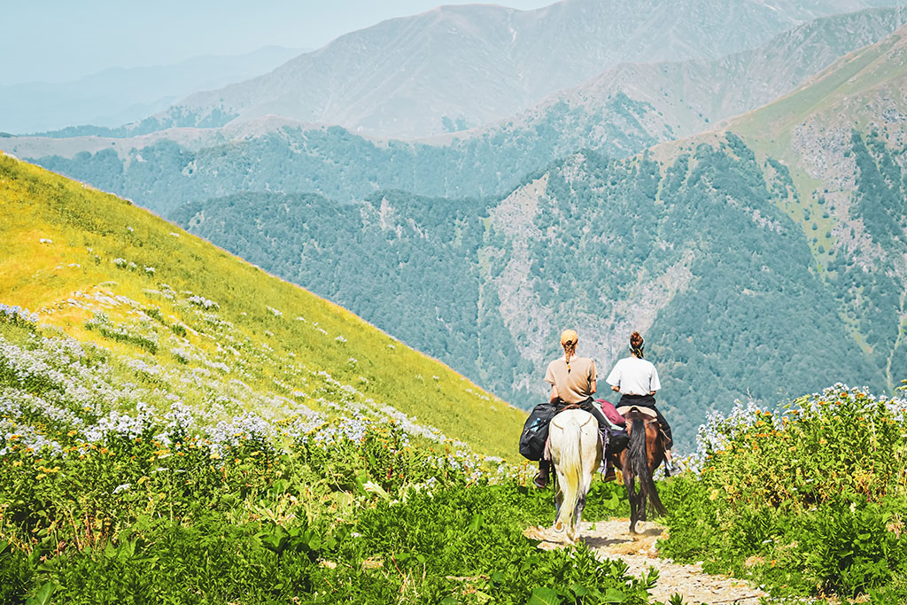 two people riding horses through the mountains. 