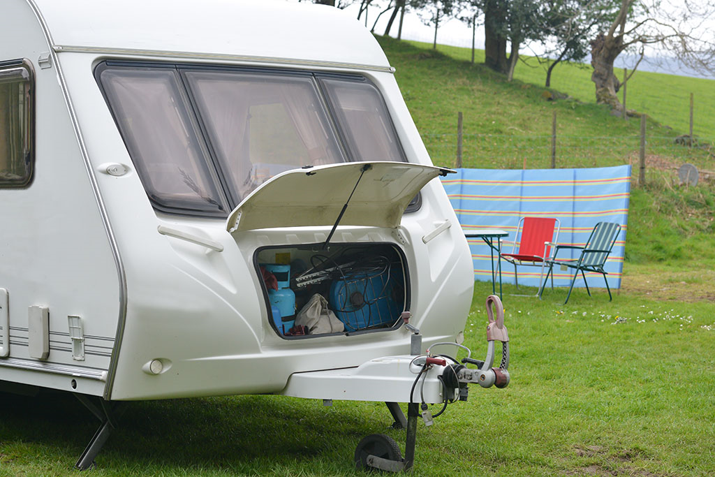 a caravan being loaded in a field with a table and chairs in the background