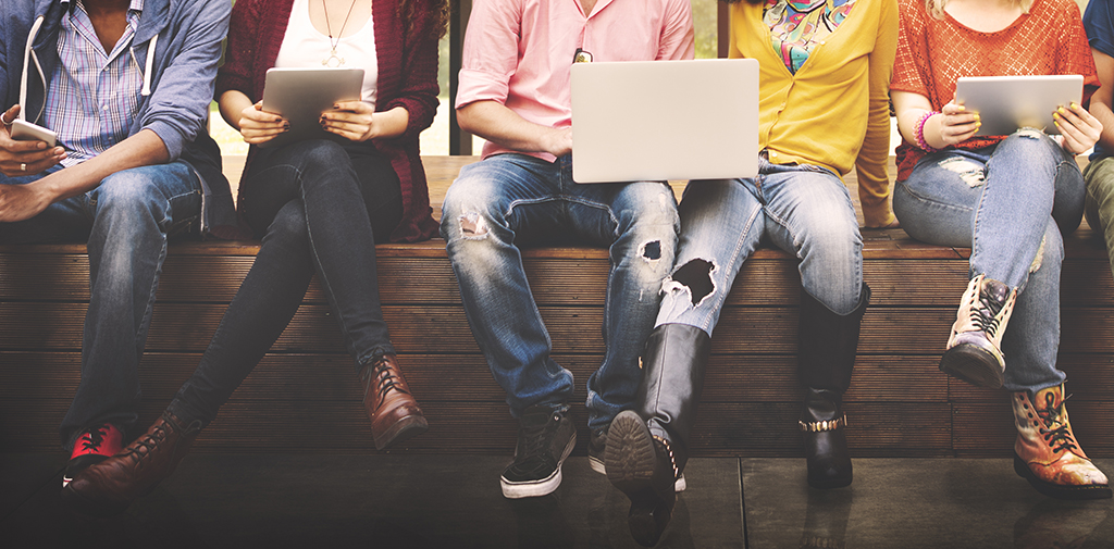 a group of students sitting on a bench looking at their laptops 