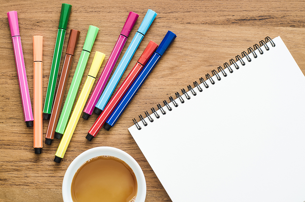coloured pens, a pad of paper and a cup of coffee on a wooden table 