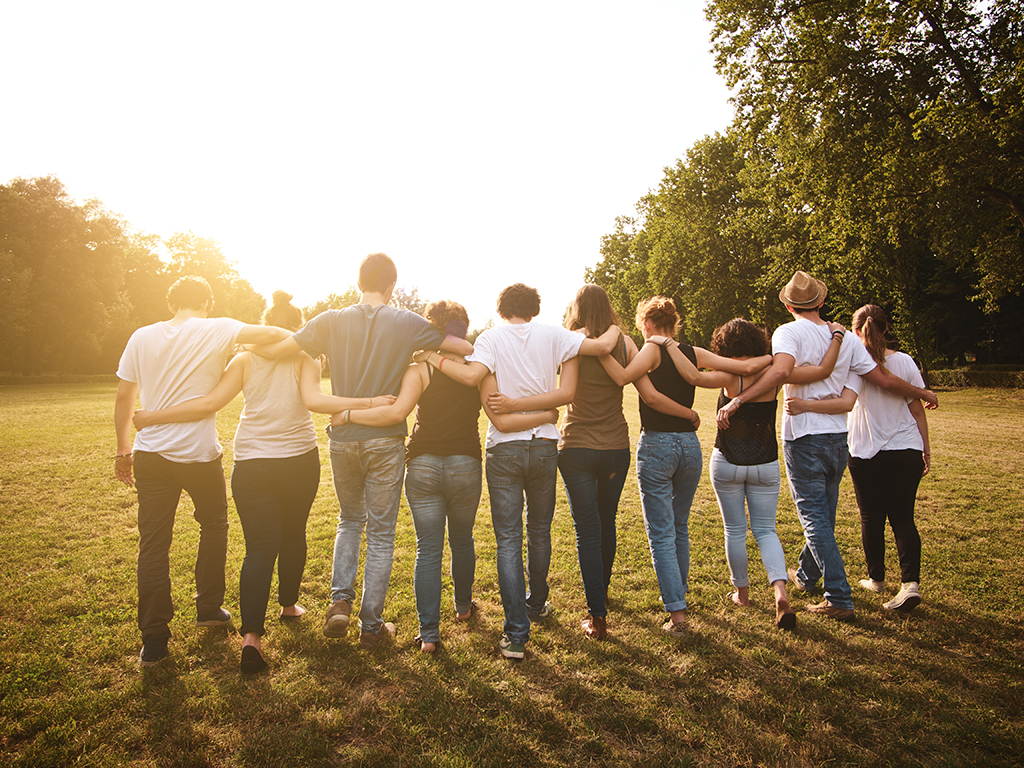 a group of people walking on grass with their arms around each other 
