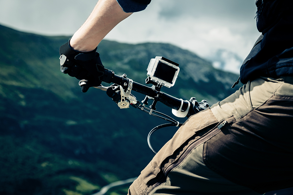 A go pro camera in action, attached to the handlebars of a bike with mountains in the background