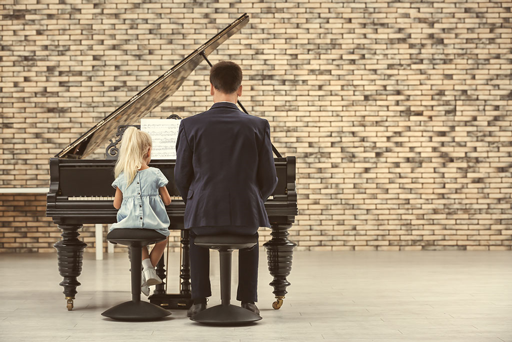 an adult sitting at a piano with his child learning  how to play together 