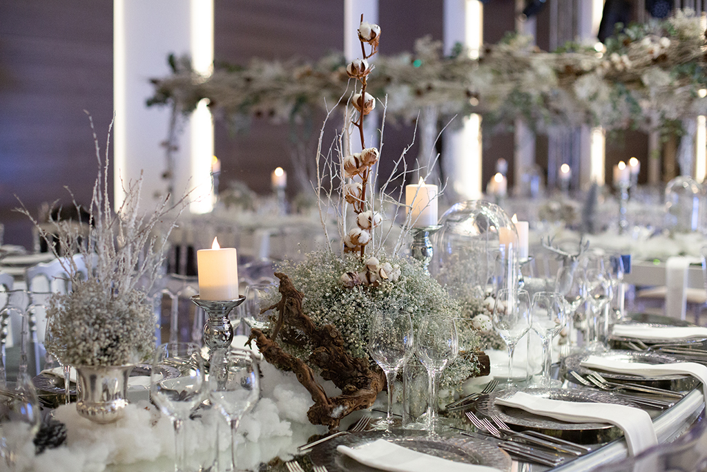a winter wedding decoration idea, a frosty centre piece on a table surrounded with candles 