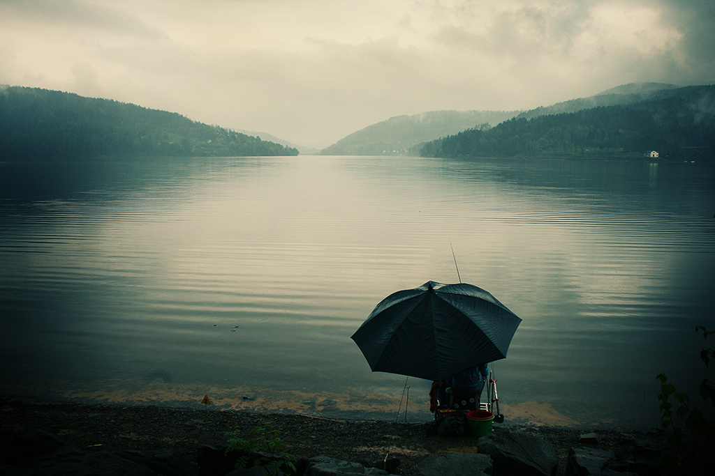 Man alone fishing during bad weather under umbrella
