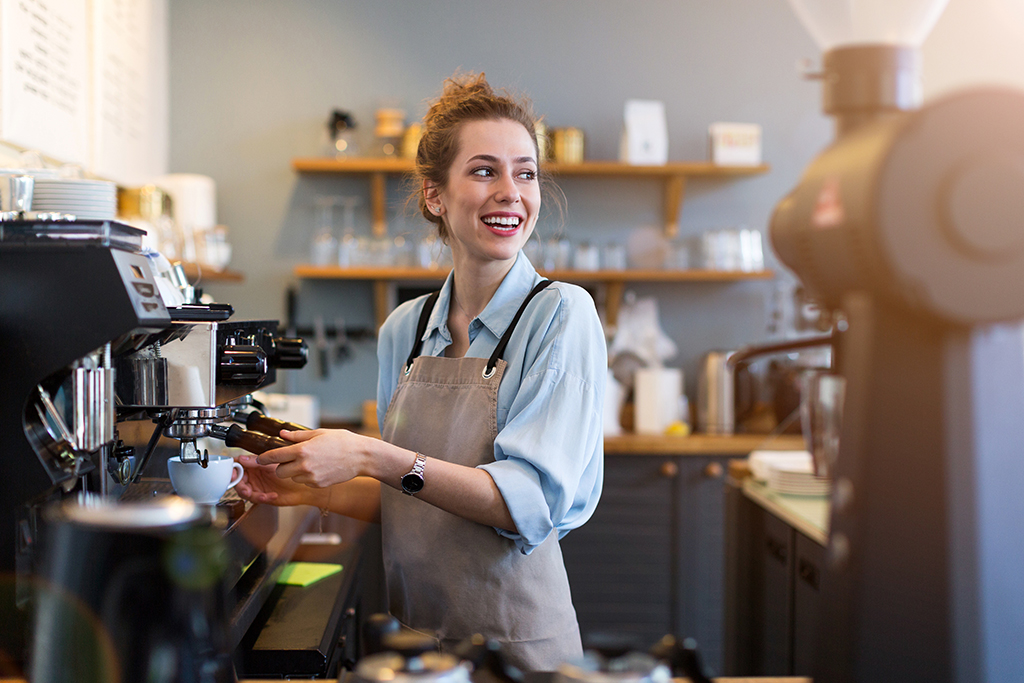 Young barista preparing coffee for customers at her cafe counter