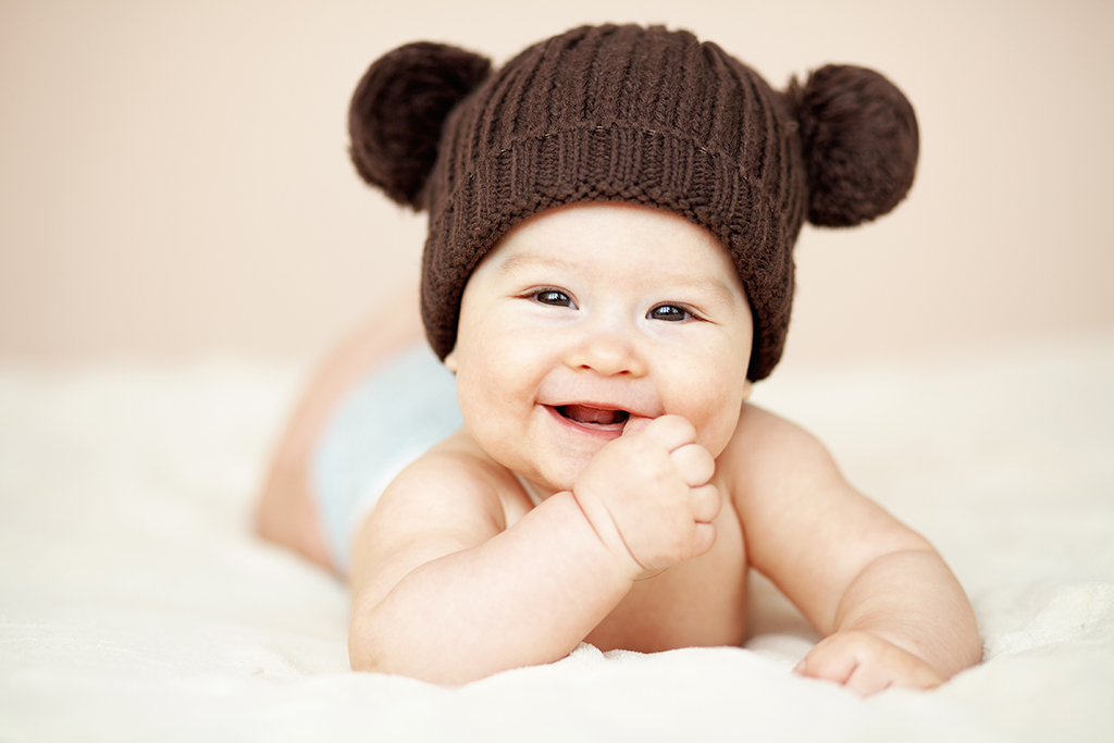 a cute smiling baby with a woolly hat on having a photoshoot at home