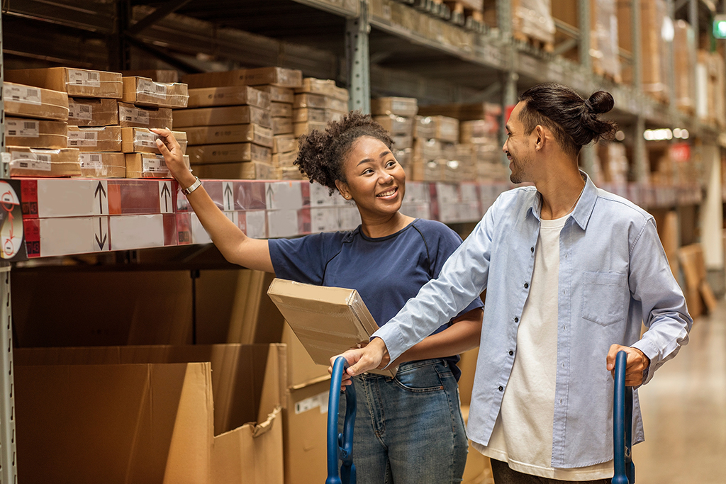 African American woman and an Asian man is couple go shopping in a warehouse, choose furniture boxes to decorate their homes and spend at self-service in wholesale.