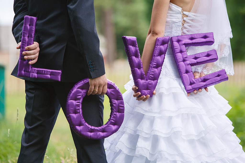 Bride and groom holding purple letters. The groom is holding L O and the bride is holding V E, to spell out love