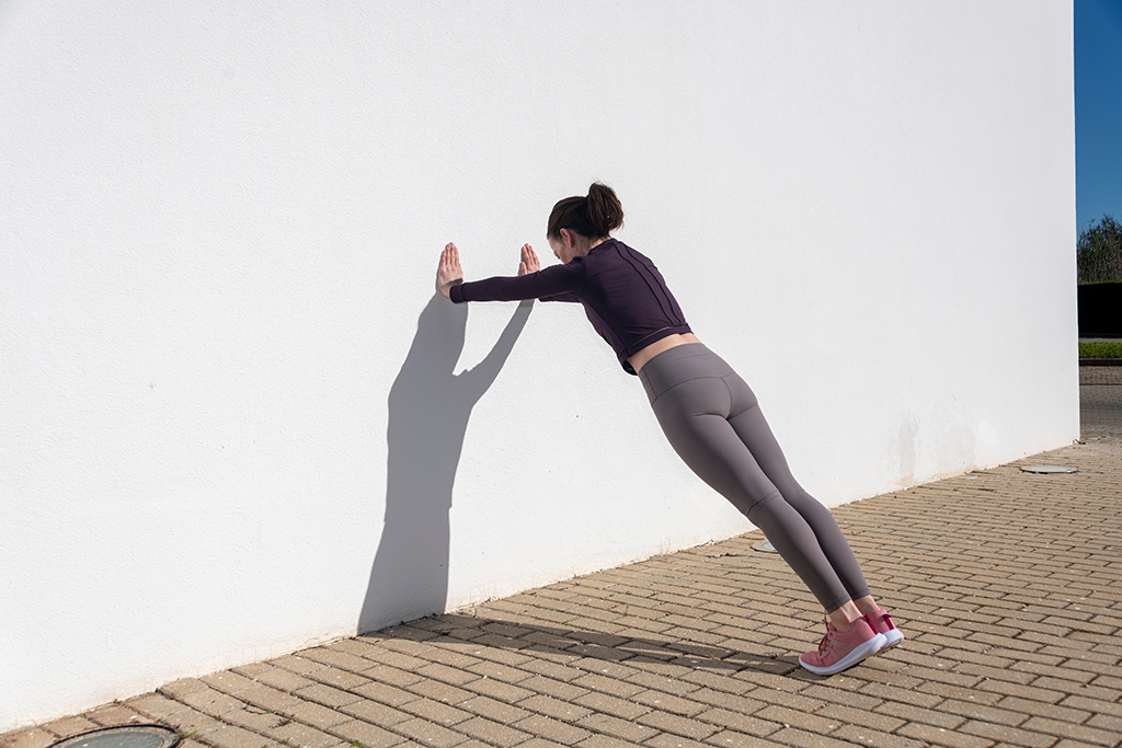 Sporty woman doing press ups against a white wall outside.