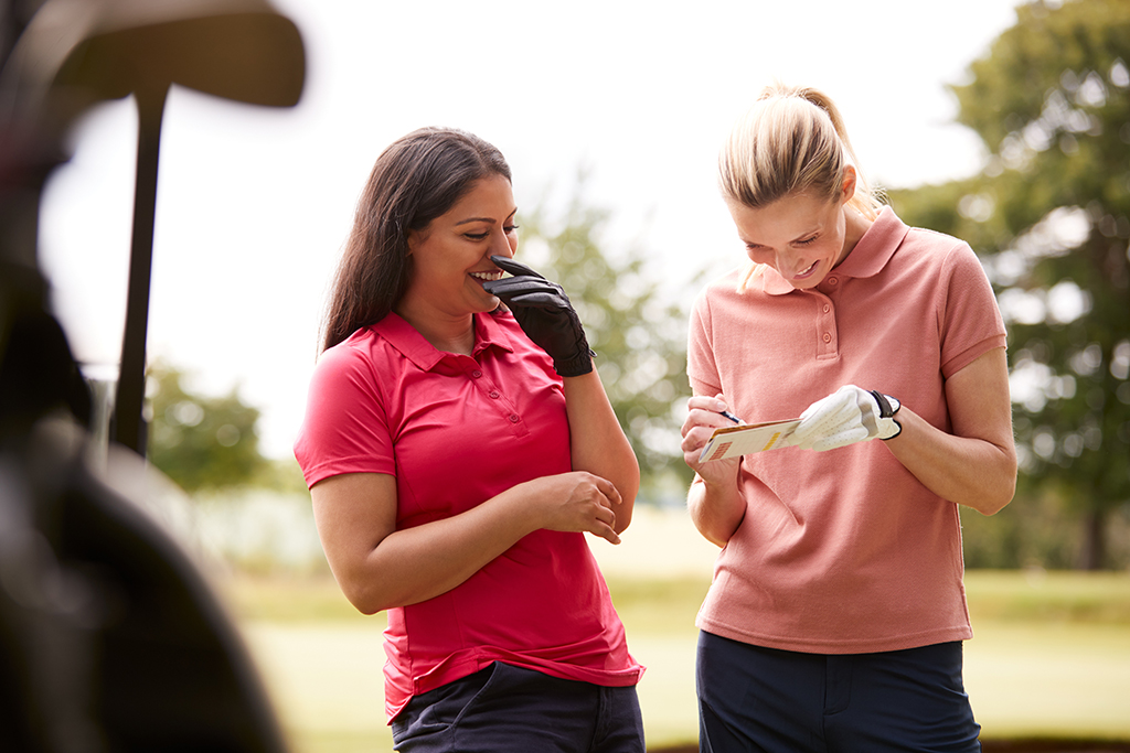 Two women making golf jokes while using a golf marking scorecard.